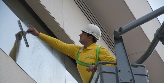 Un operario de Brócoli en una grúa limpiando una ventana de un edificio