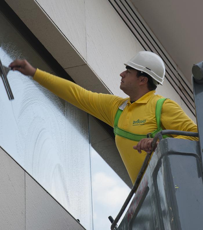 Un operario de Brócoli en una grúa limpiando una ventana de un edificio